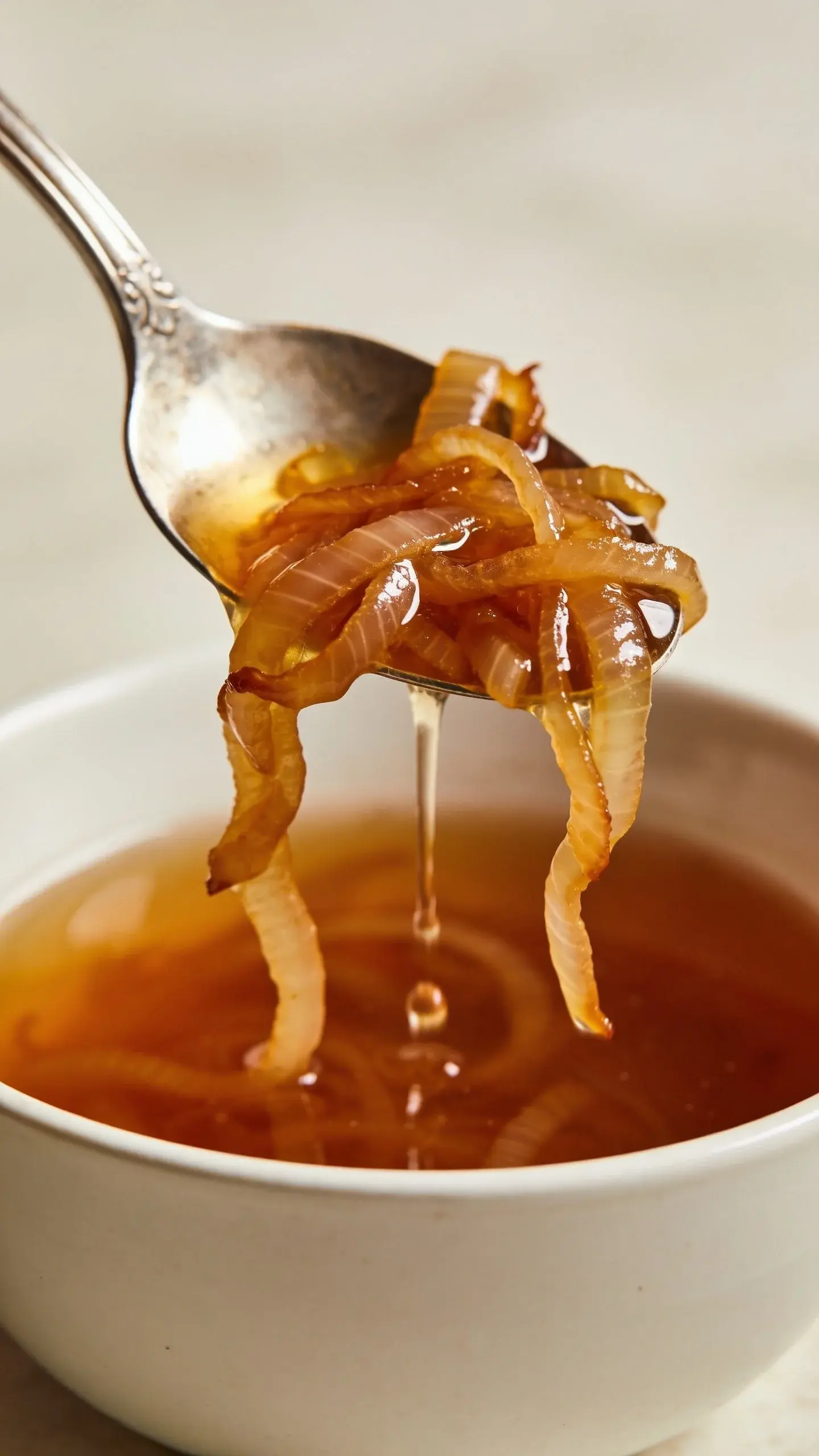 Spoon lifting caramelized onions and amber broth from a bowl of French onion soup