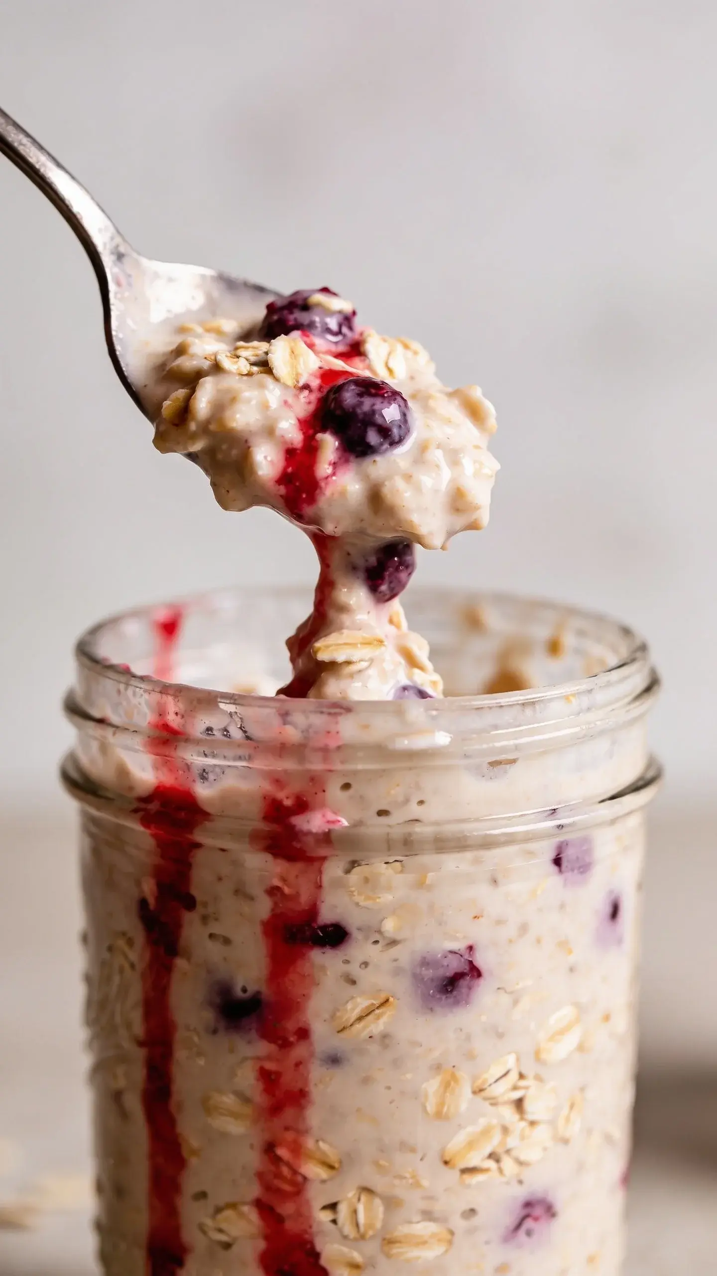 Spoonful of triple berry overnight oats with berry sauce above the jar