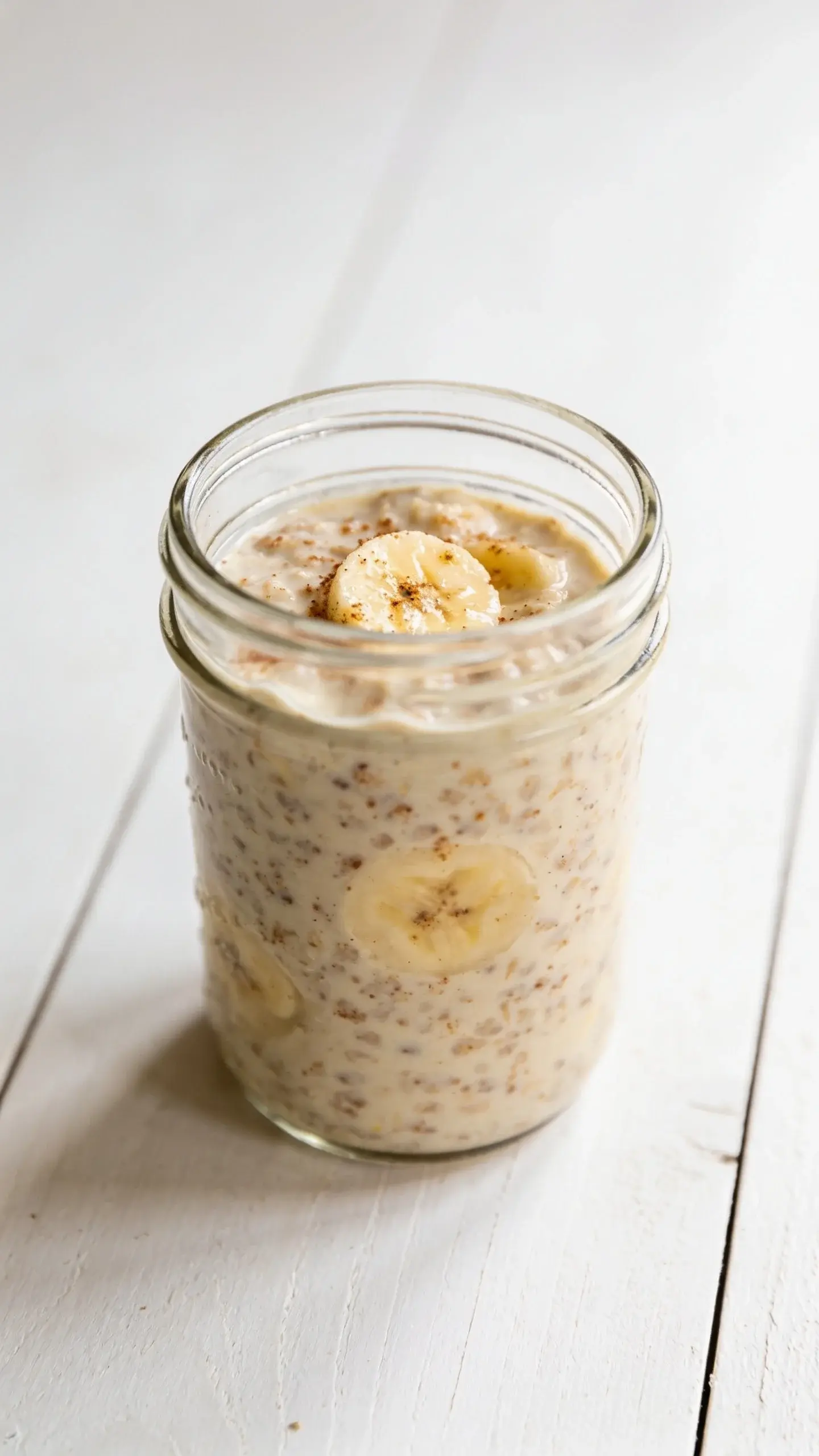 Glass jar of banana bread overnight oats topped with banana slices and cinnamon on a wooden table