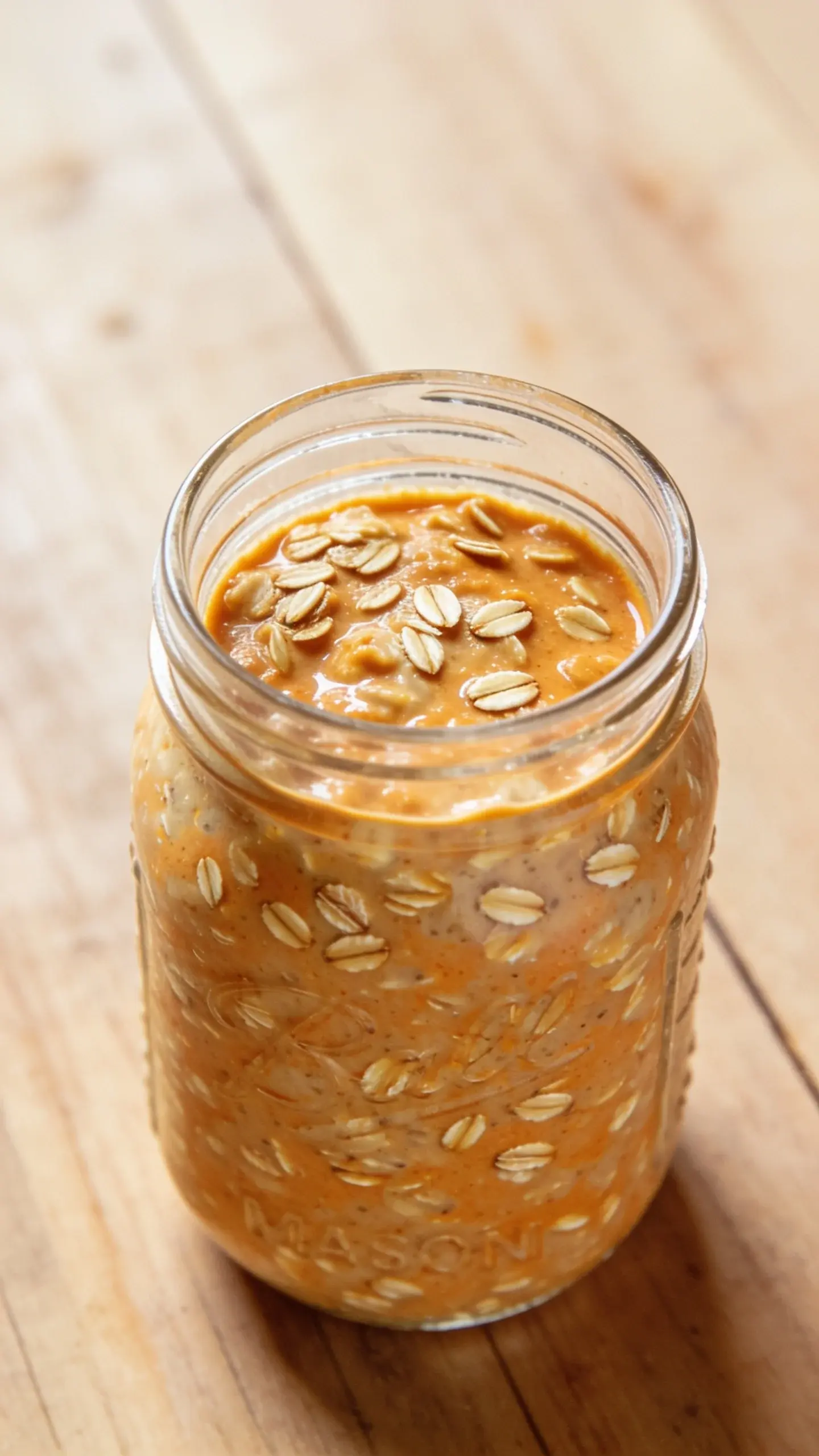 Glass jar of creamy pumpkin pie overnight oats with a dusting of cinnamon on a wooden table