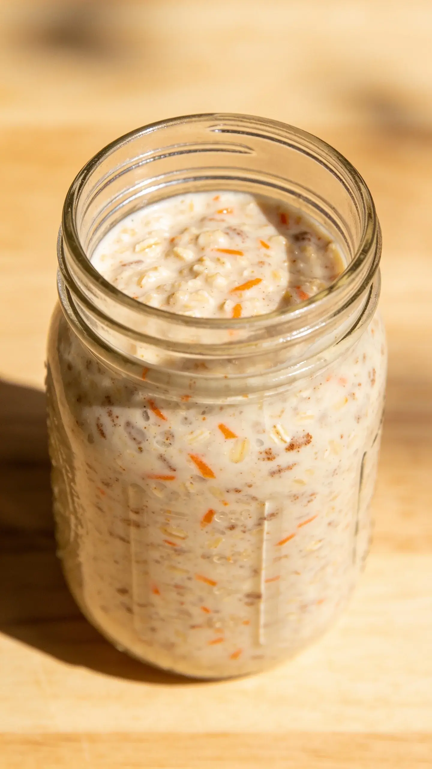 Glass jar of carrot cake overnight oats with grated carrot and cinnamon on a light table